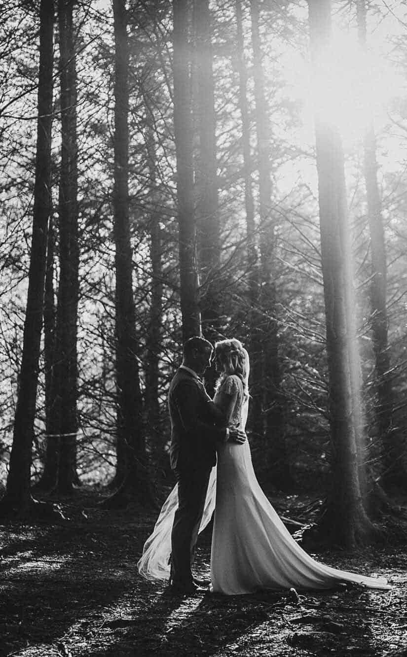 Ireland elopement in a forest - black and white - Winter sun shining through the trees, couple holding each other